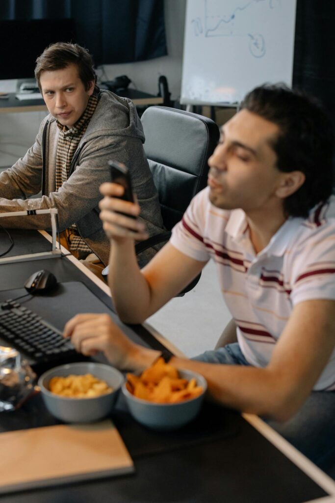 Programmer Looking with Disapproval at His Colleague Playing with a Smartphone